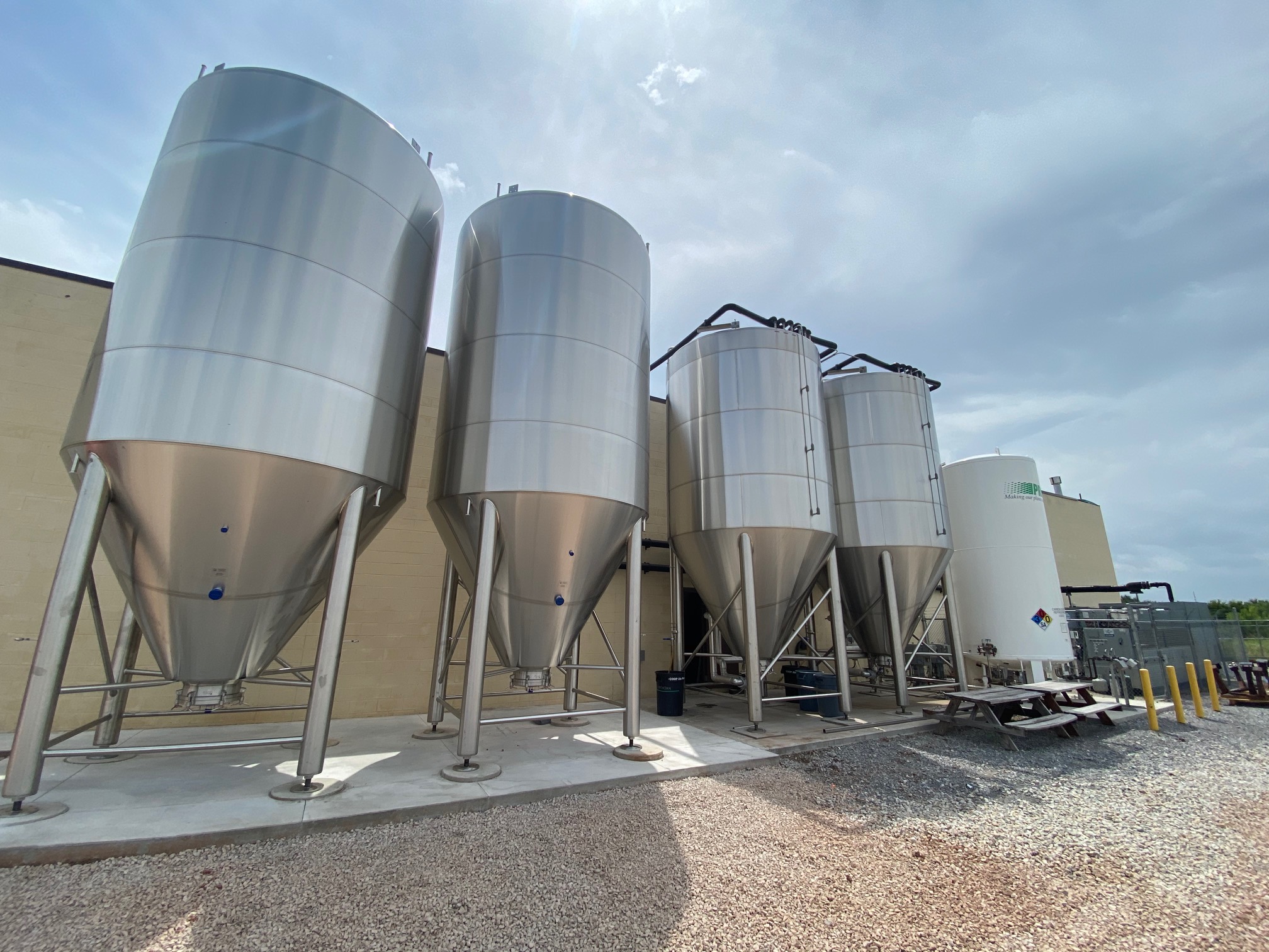 Four large brewery tanks lined up outside a yellow building.